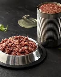 Raw minced meat in a bowl beside stacked cans, wet cat food ingredients